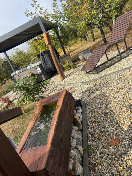 A jacuzzi a pergola alatt, mellette a napozóágy és a csobogó – a Ficak vendégház kertje
